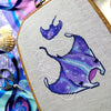 Slight closeup and angled view of ocean rays cross stitch pattern. Cross stitch pattern is of small to medium size. White bubbles are minimalist. Colors are vibrant and beautiful. Rays are soaring through the water.