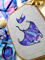  Slight closeup and angled view of ocean rays cross stitch pattern. Cross stitch pattern is of small to medium size. White bubbles are minimalist. Colors are vibrant and beautiful. Rays are soaring through the water.