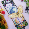 Angled front view of Art Nouveau barn owl cross stitch pattern. Finished piece is elongated and looks like a window. There is a big blue moon in the middle that radiates outward. A barn owl is flying into the scene with its wings spread.