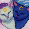 Slightly zoomed in view of Smitten Kittens. The cat on the left is white with a sun on his forehead, the cat on the left is blue with a moon on his forehead. Their noses and earsare bright pink. The scene contains a lot of soft, vibrant colors.
