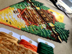 Closeup of the Lakeside Cabin cross stitch pattern. Image is zoomed in on the lower end of the design, where the water reflection is visible. The colors are vibrant, the stitches are neat and uniform. In the forefront are the rim of a hat and bobbins