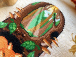 Closeup of Sleeping Fox upper area. Design is framed by trees and mushrooms. Leaves are on the ground. Two sun rays break through the trees on the lefthand side. A yellow and orange sky can be seen in the back. Trees are different colors.