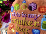 Closeup of the Trinket Bag. Individual stitches are clearly visible. The colors are mainly brown, gold, purple, blue, red and yellow. Font reminds of adventure books or medieval times.