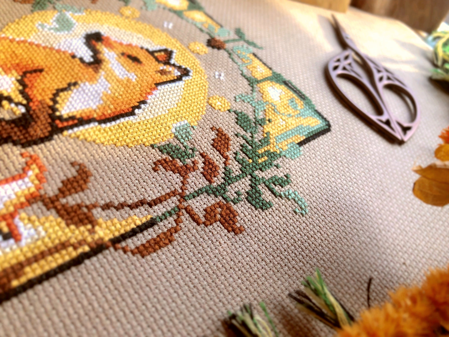 Close-up of Art Nouveau Fox cross stitch pattern. Individual stitches visible. Embroidery scissors in the background. Texture of the fabric is visible too - this is 16ct Aida by Permin of Copenhagen.